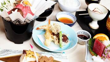 A variety of Japanese dishes including sashimi, tempura, and a selection of vegetables and meats, served on a table with multiple bowls and plates.