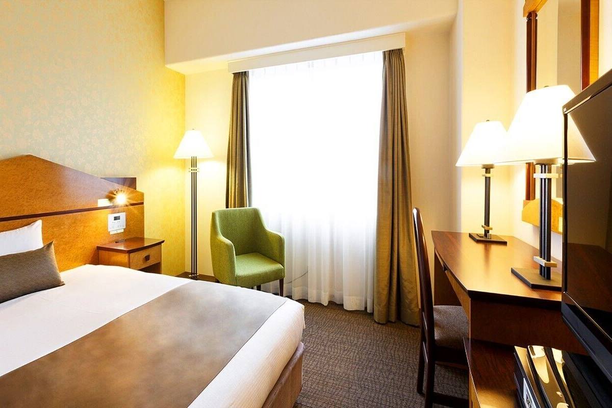 A hotel room with a large bed, a desk, a chair, and two lamps.