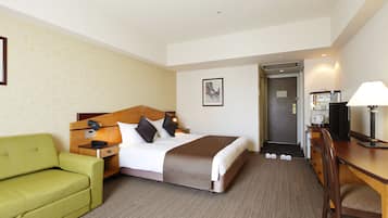 Habitación de hotel con una cama, un sofá verde, un escritorio con lámpara y un televisor.