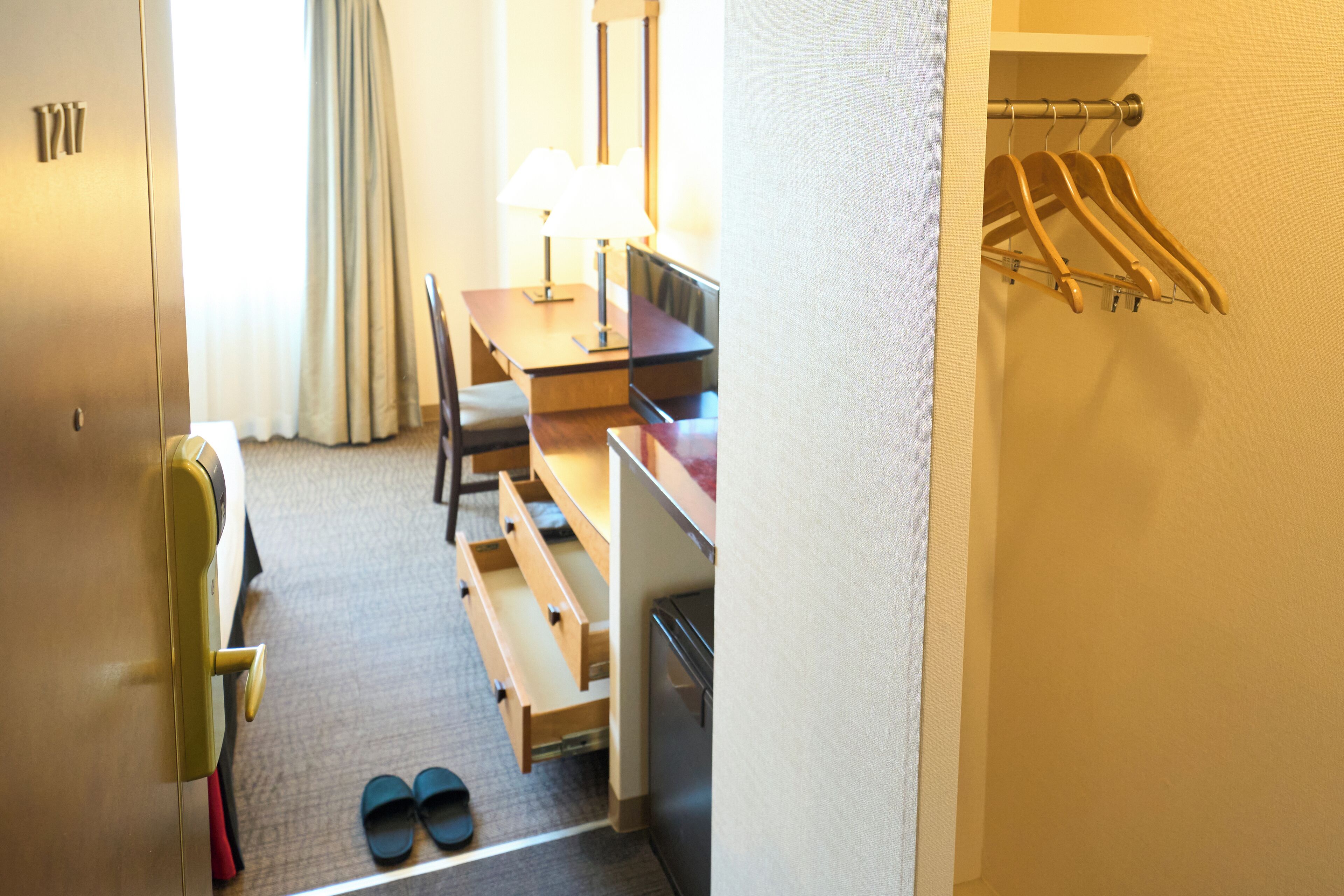 Habitación de hotel con escritorio, silla y perchero con colgadores.
