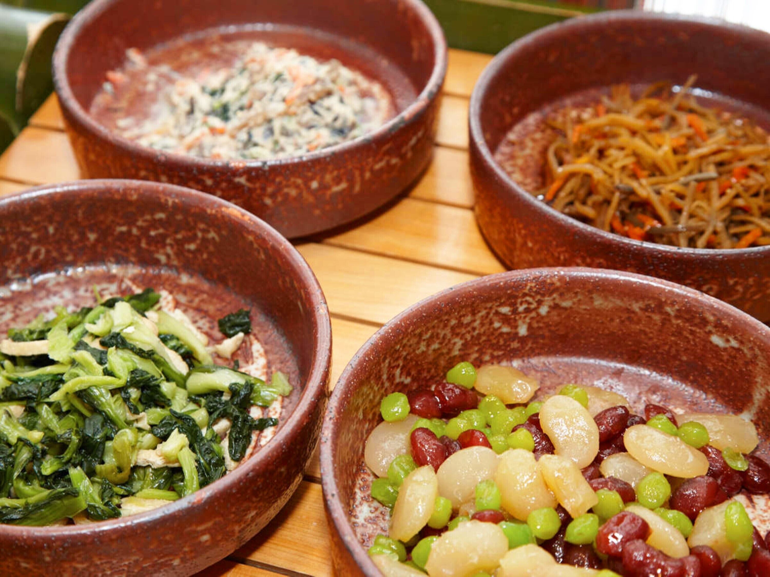 Four bowls of food on a wooden table.