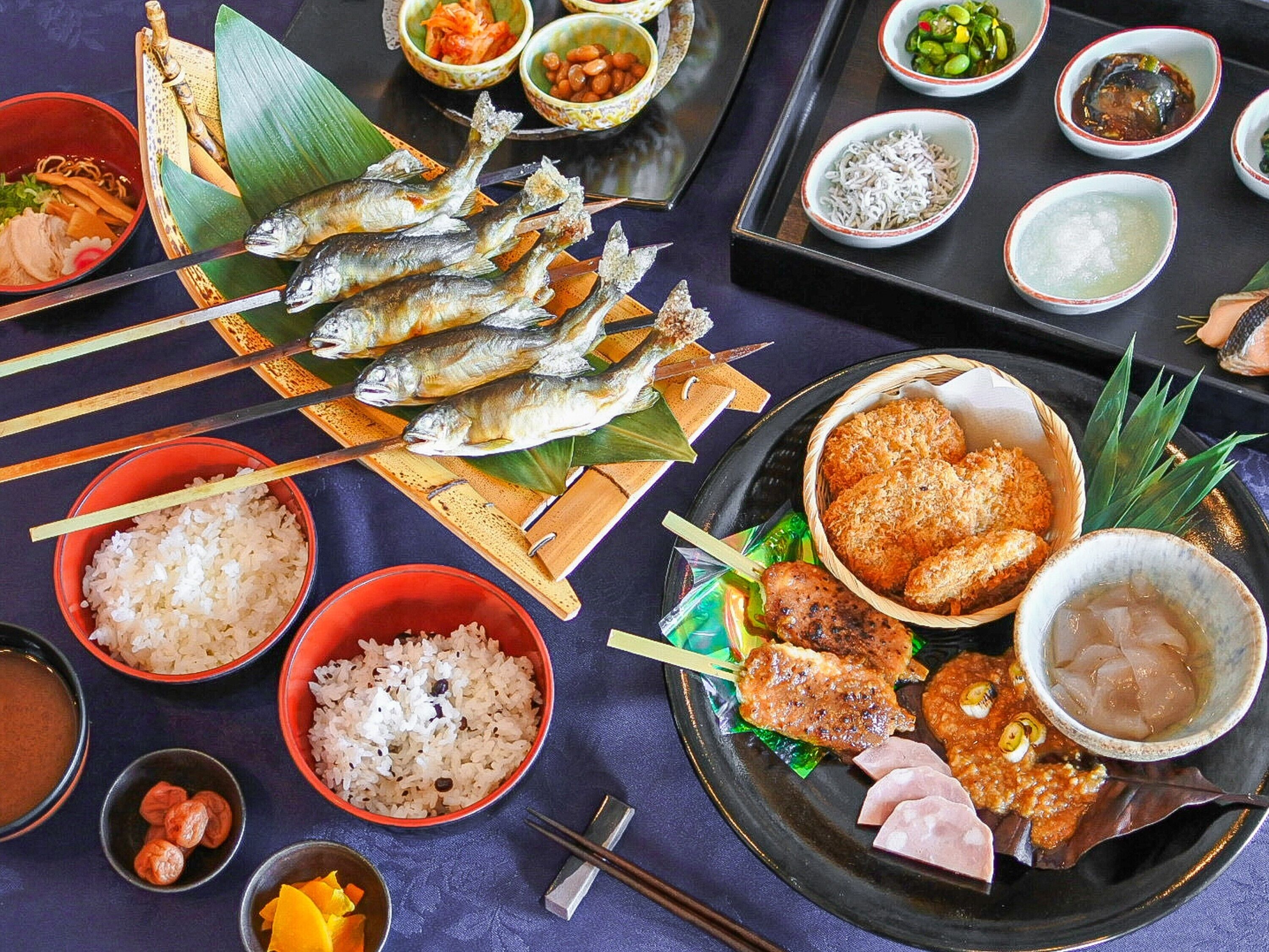 Une variété de plats, notamment du poisson grillé, du riz et d’autres accompagnements, sont disposés sur une table.
