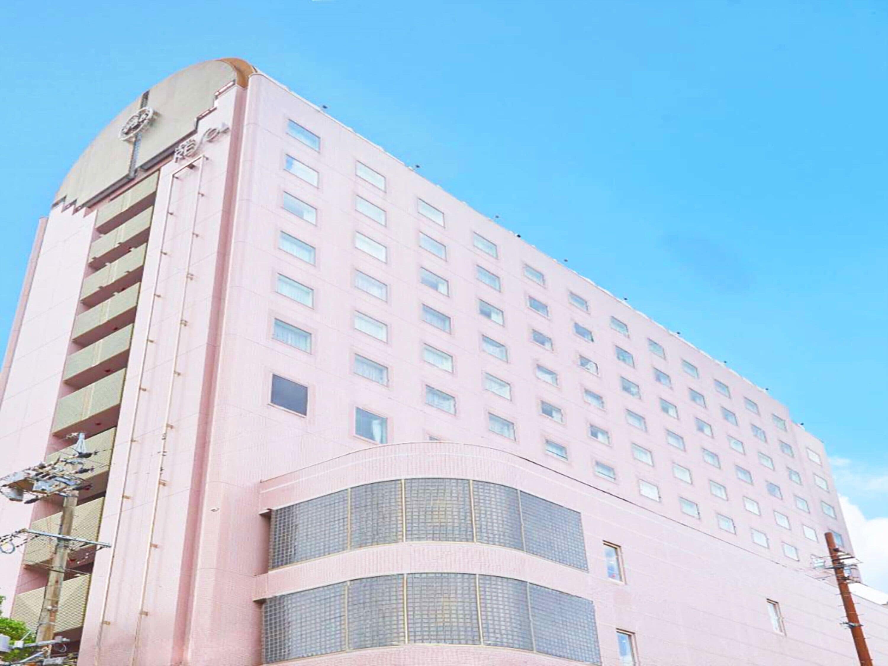 A tall pink building with multiple floors, large windows, and a curved section near the bottom.