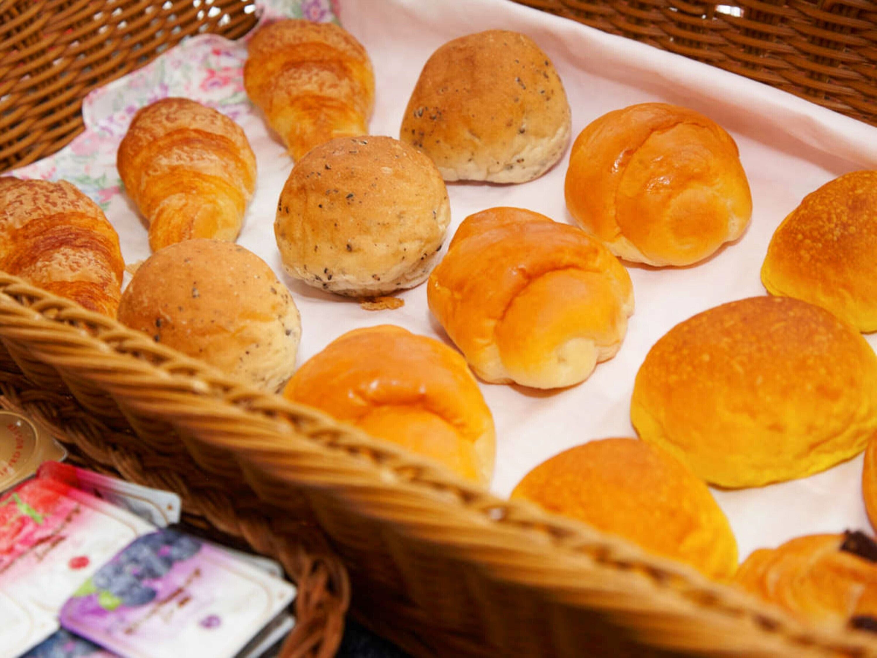Een mandje met verschillende soorten broodjes, waaronder croissants en Kaiserrolletjes, op een witte papieren handdoek.