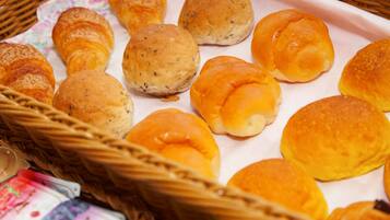 Een mandje met verschillende soorten broodjes, waaronder croissants en Kaiserrolletjes, op een witte papieren handdoek.