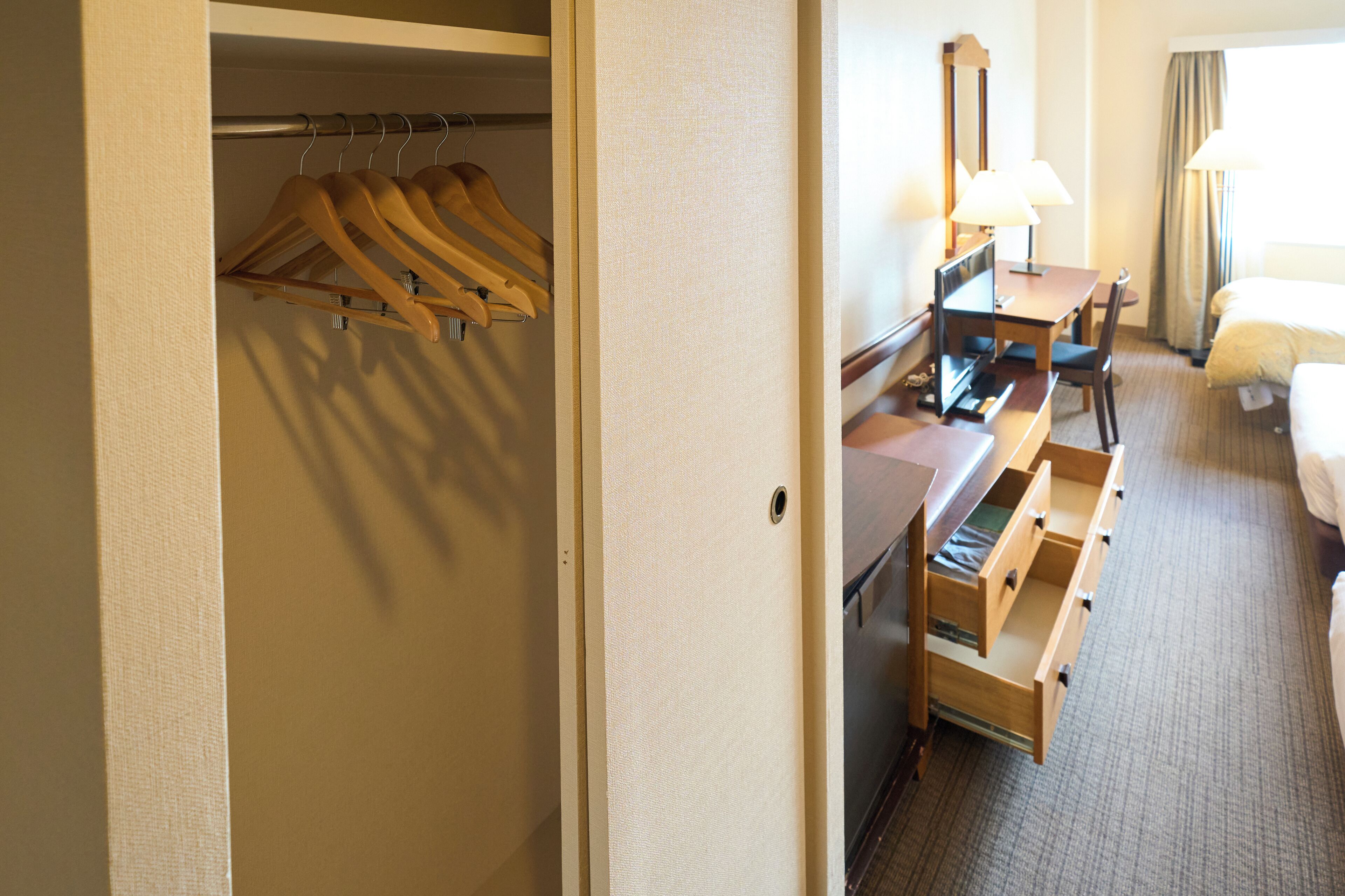 A hotel room with a walk-in closet, a desk with a chair, a bed, and a bathroom.