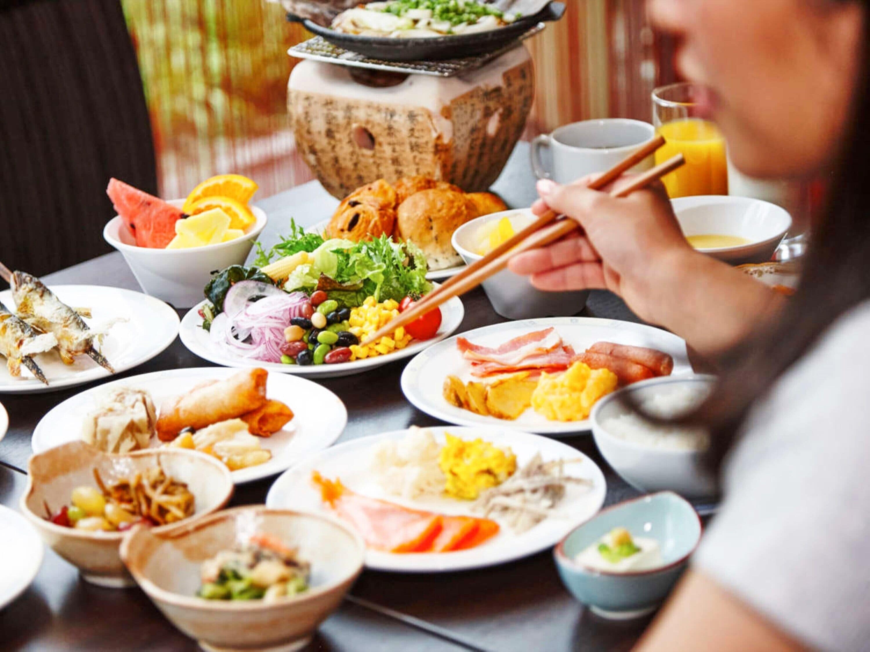 Una mesa de comedor con varios platos, incluyendo pescado, ensalada y huevos, y una olla caliente al fondo.