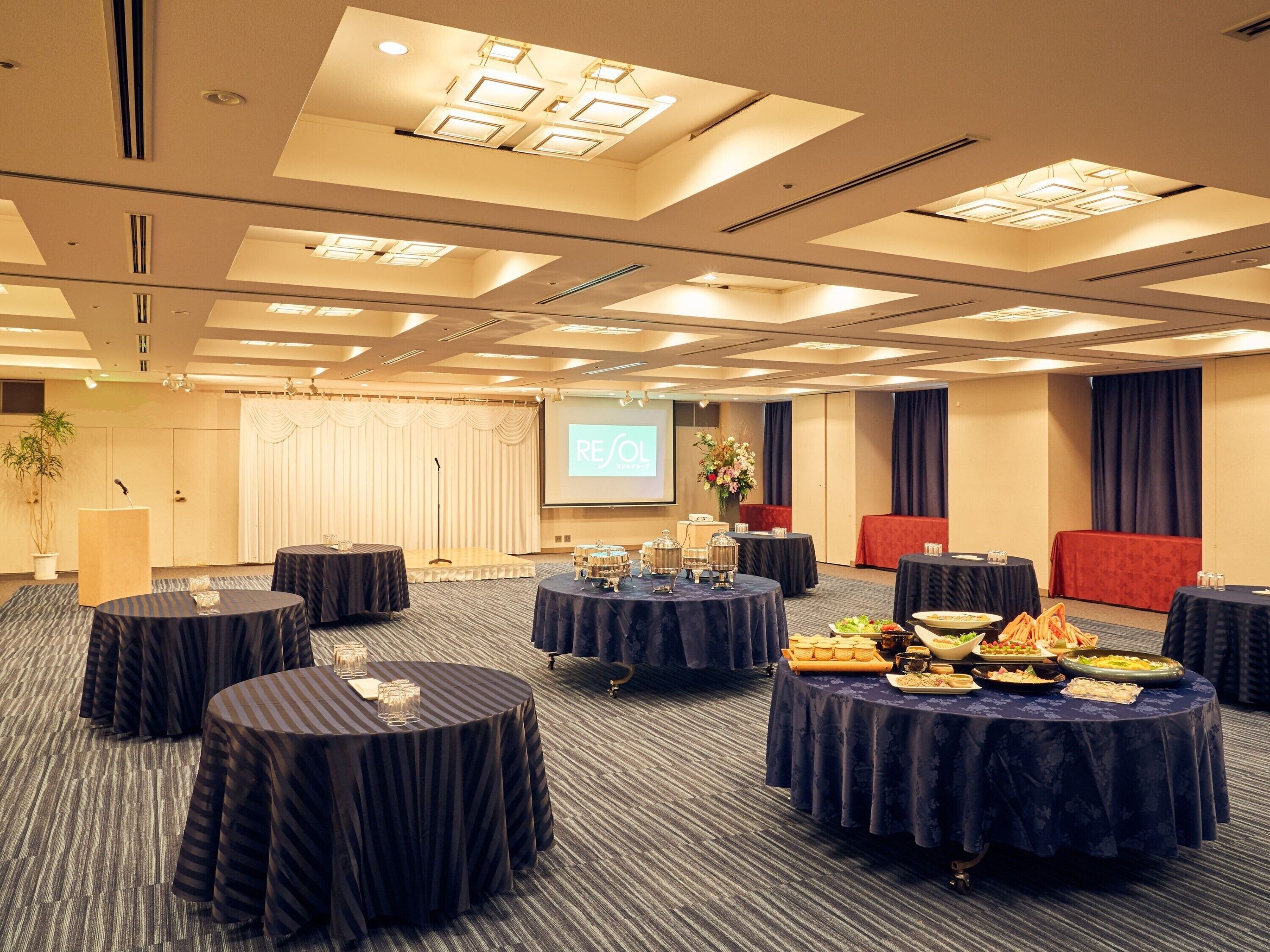 A conference room with multiple round tables, a stage with a podium, and a screen displaying "RESOL".