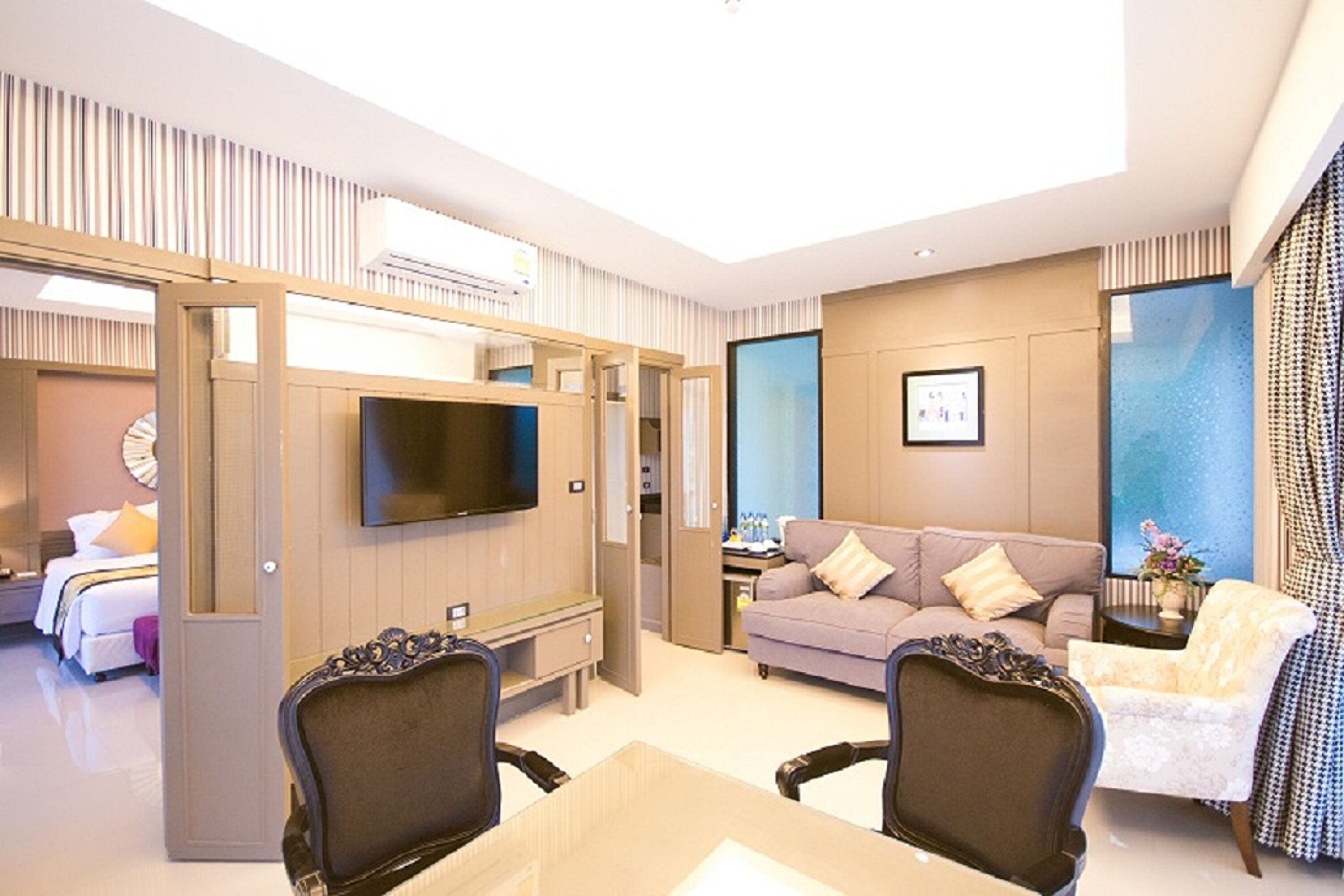 A hotel room with a TV, a sofa, a dining table, and a chair.