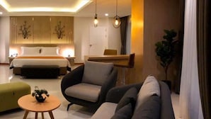 Une chambre d’hôtel moderne avec un grand lit, deux fauteuils, un canapé, une petite table ronde et une plante en pot.