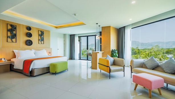 Une chambre d’hôtel moderne équipée d’un lit, d’un canapé, d’une chaise, d’un bureau et d’une grande fenêtre donnant sur un paysage agréable.