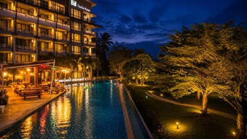 A hotel with a swimming pool, outdoor seating, and well-lit surroundings.