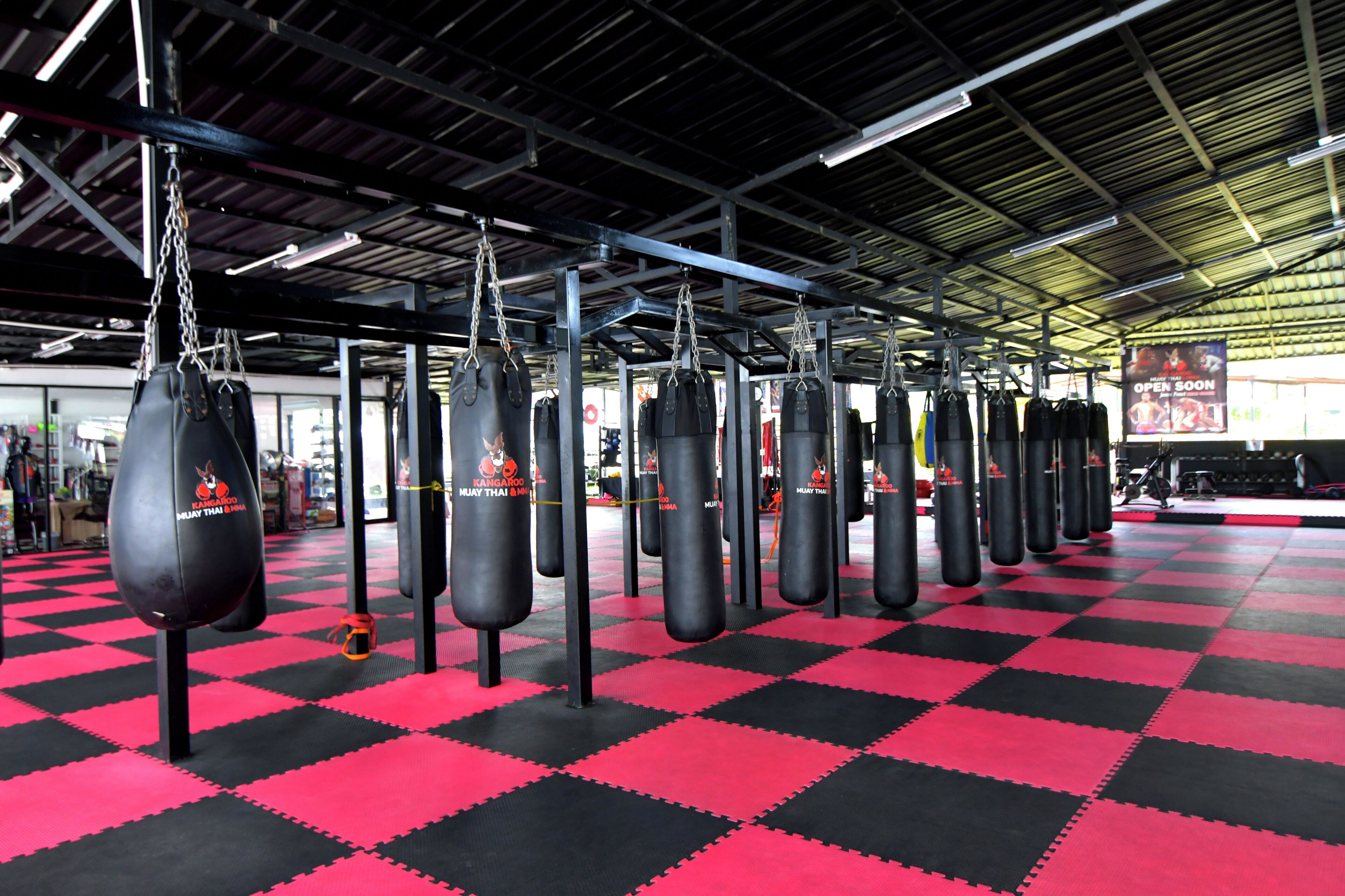 Un gimnasio con piso a cuadros negro y rojo, múltiples sacos de boxeo y un cartel que indica que abrirá pronto.