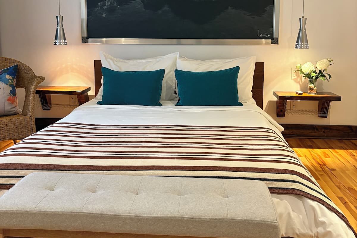 Un dormitorio con una cama grande, dos mesitas de noche, un aire acondicionado de pared y un cuadro de rocas.