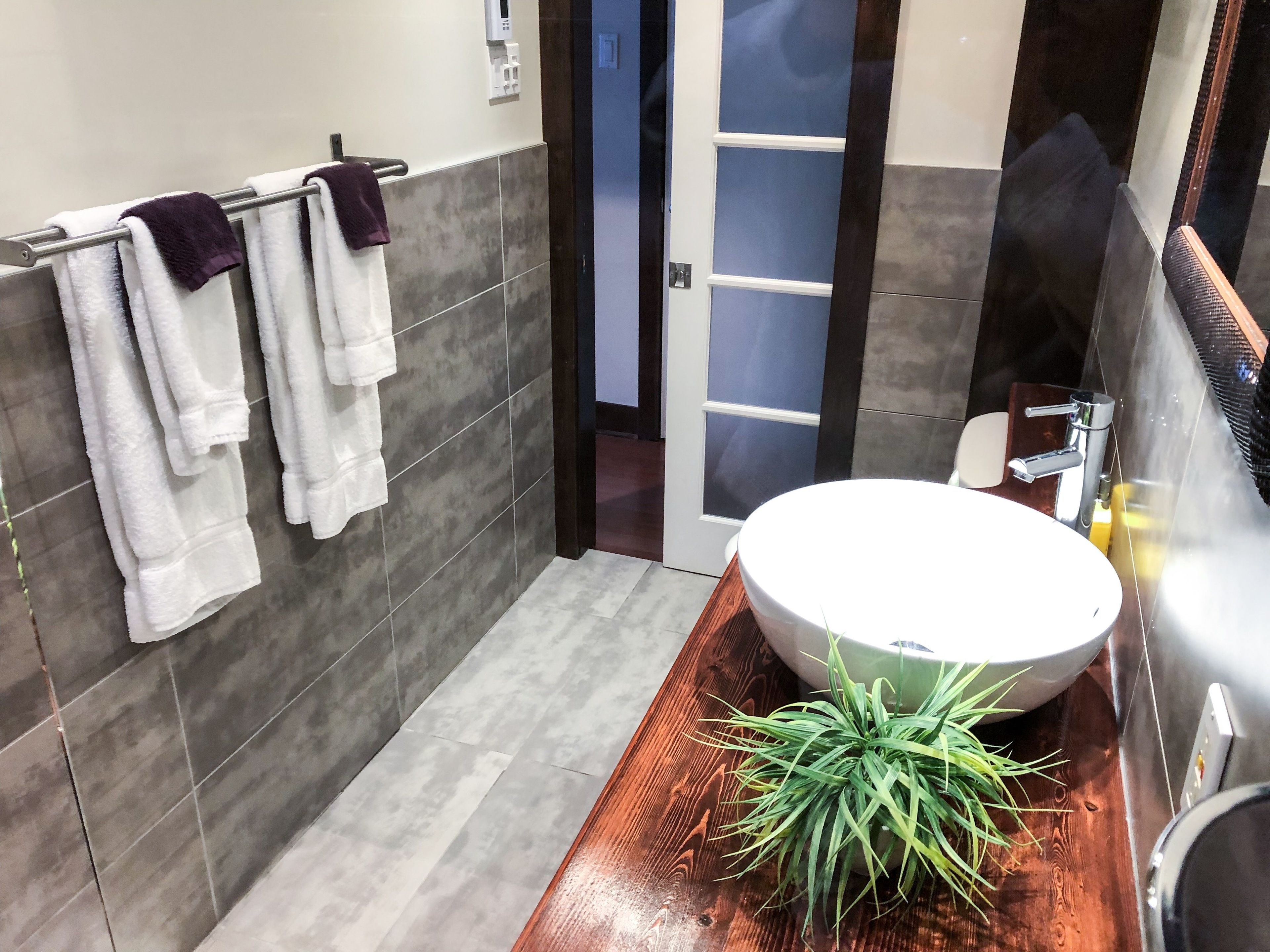 A modern bathroom with a large white sink, a wooden vanity, and a potted plant.