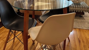 A dining area with a glass table, black and white chairs, a sofa with cushions, and abstract paintings on the wall. - Loft Jacques-Cartier- Le Plateau Free Parking (Montreal)