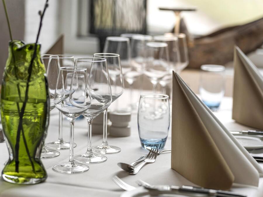 A dining table set with multiple wine glasses, a green vase, and neatly arranged cutlery.