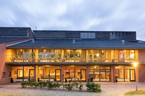 Un bâtiment à deux étages doté d’un balcon, d’un espace extérieur aménagé pour s’asseoir et d’une façade en briques.