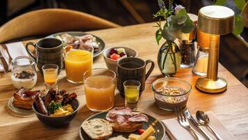 Een ontbijtsetting met diverse etenswaren, drankjes en een koffiezetapparaat op een houten tafel.
