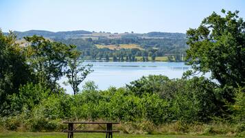 Uma mesa para piquenique em um campo gramado, com um lago e colinas ao fundo.