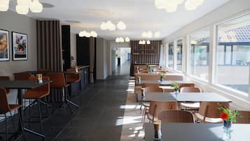 Un restaurant moderne avec un long comptoir, de nombreuses tables et des chaises. Il y a des luminaires au plafond et de grandes fenêtres.