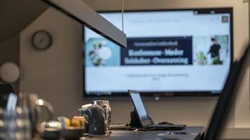 A laptop on a desk with a coffee mug, a bowl of fruit, and a clock on the wall.