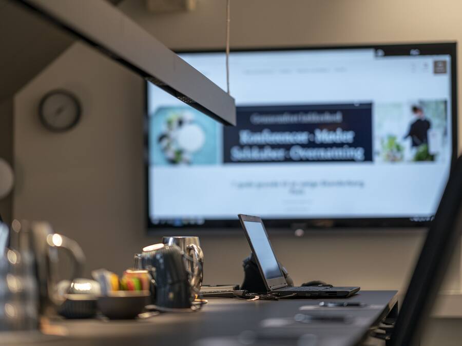 A laptop on a desk with a coffee mug, a bowl of fruit, and a clock on the wall.