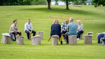 A group of people sitting on stone stools in a grassy field with trees in the background.