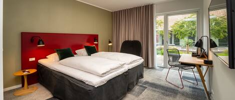 A modern hotel room with a large bed, a desk, and a view of the outdoors.