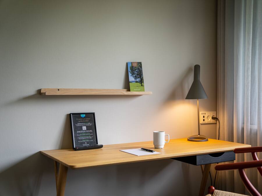 Un bureau en bois sur lequel se trouvent une tasse blanche, un certificat encadré et une petite plante posée sur une étagère.