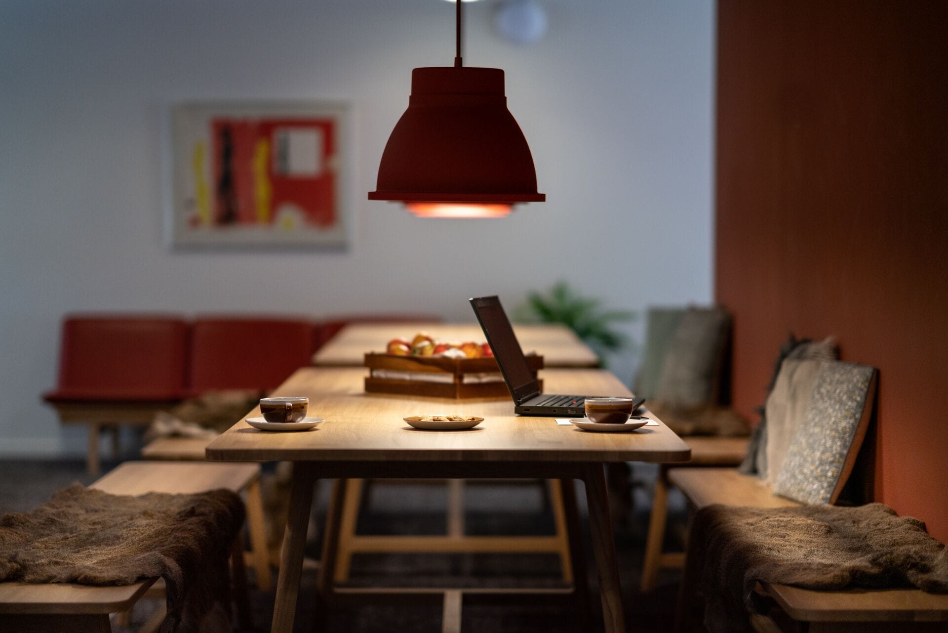 A dining area with a wooden table, red chairs, a laptop, and a hanging red pendant light.