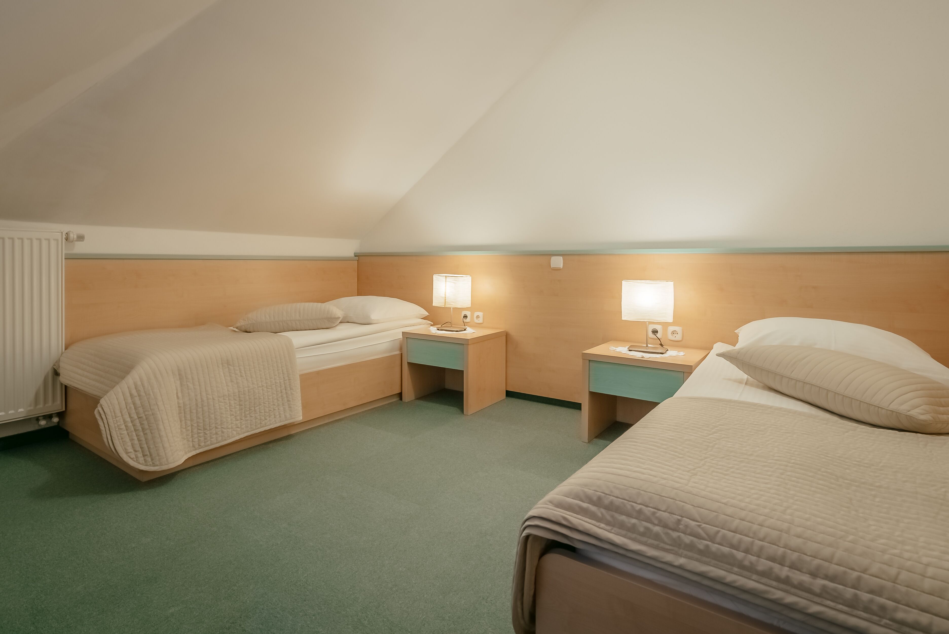 A hotel room with two single beds, each with a bedside table and lamp, and a large bed with a pillow.