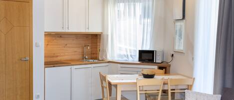 Eine kleine Küche mit weißen Schränken, einer Holz Arbeitsplatte und einem Essbereich mit Tisch und Stühlen.