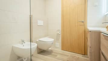 Un baño moderno con cabina de ducha de vidrio, puerta de madera, lavabo blanco y un inodoro.