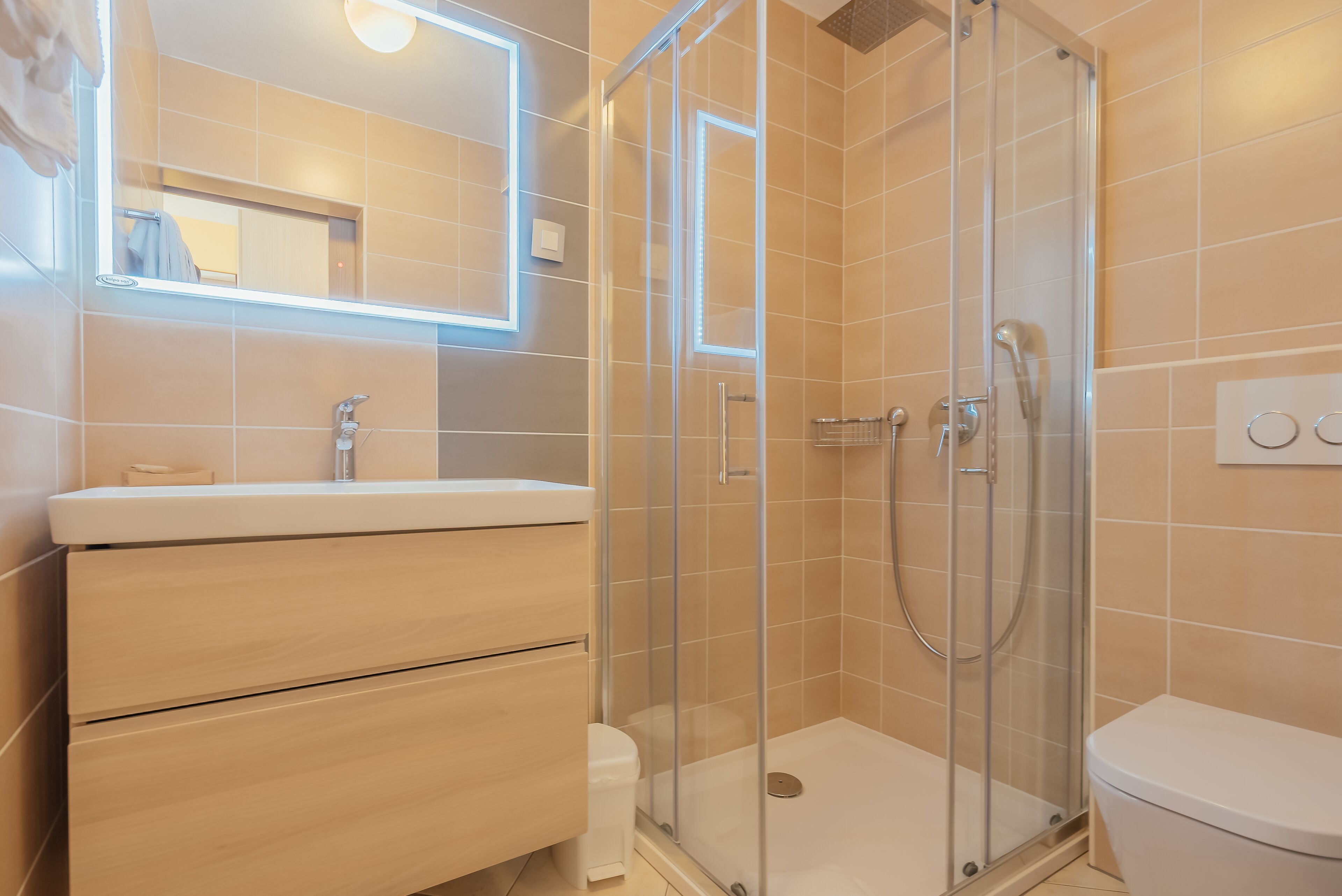 Une salle de bain moderne avec une douche à parois de verre, un lavabo blanc et un miroir au-dessus du meuble-lavabo.