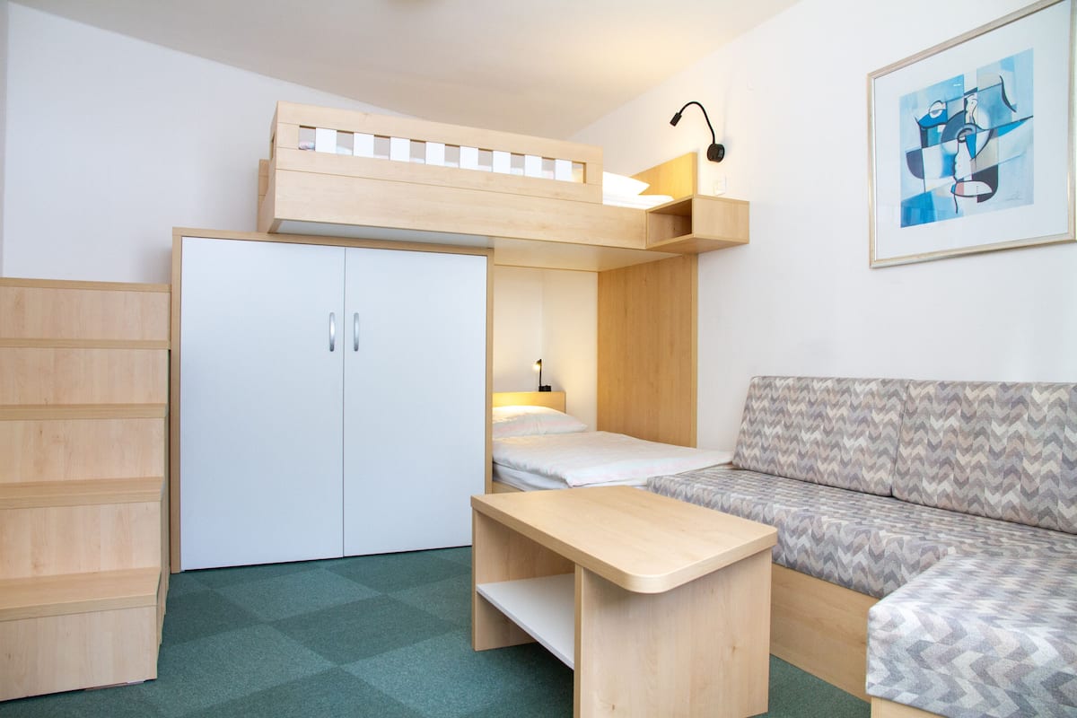 A compact room with a bunk bed, a desk, a sofa, and a wardrobe.