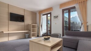 Una sala de estar moderna con un televisor de pantalla plana, un sofá gris, una mesa de centro de madera y vistas a montañas a través de ventanas amplias.