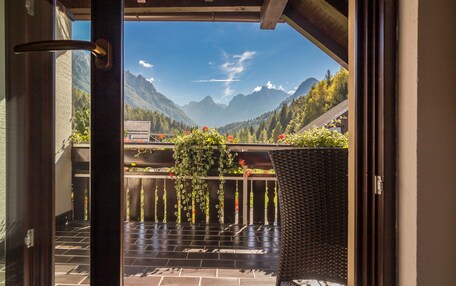 A balcony with a view of mountains, a wicker chair, and a hanging plant.