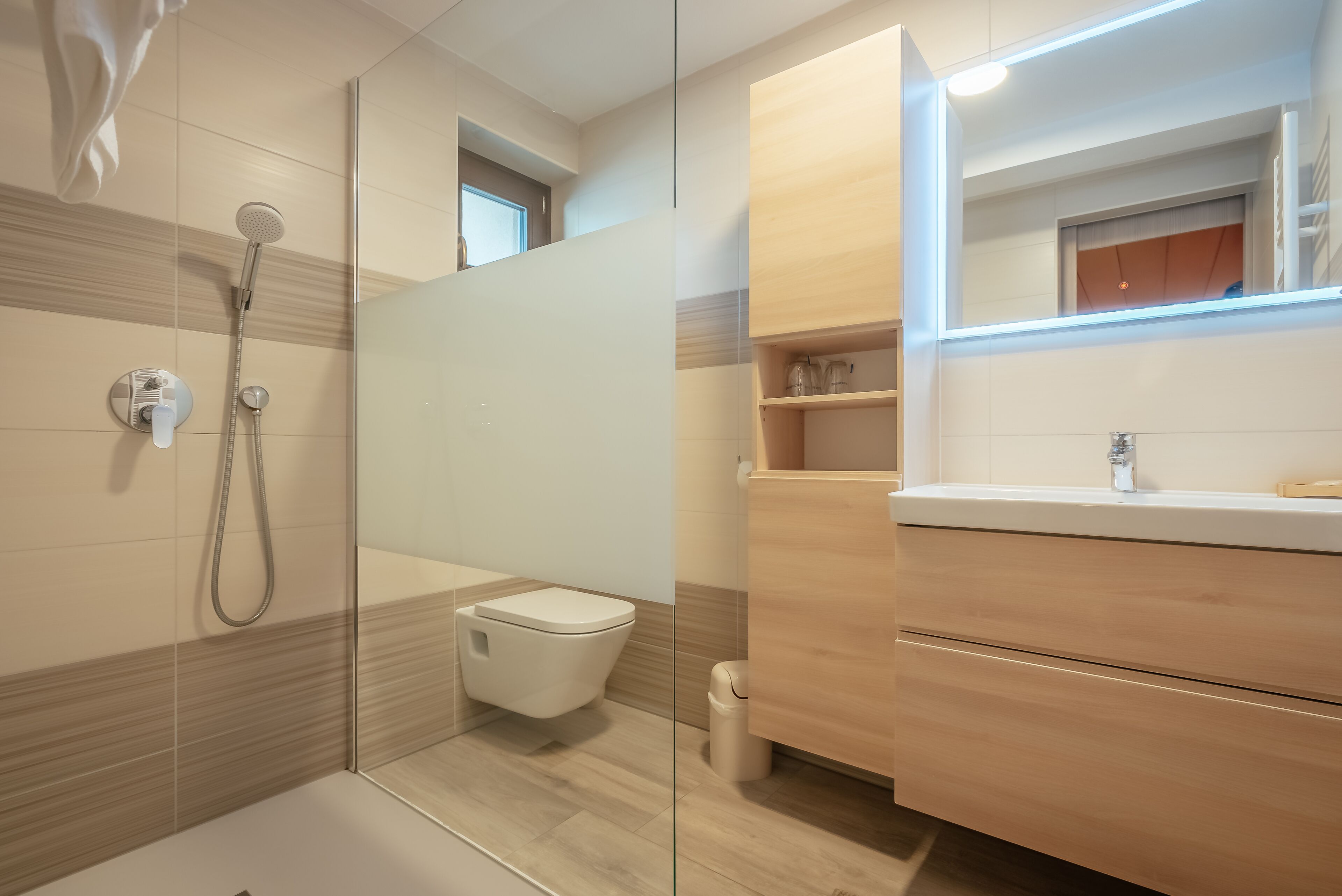 Une salle de bain moderne équipée d’une douche, de toilettes et d’un meuble-lavabo en bois avec un miroir.