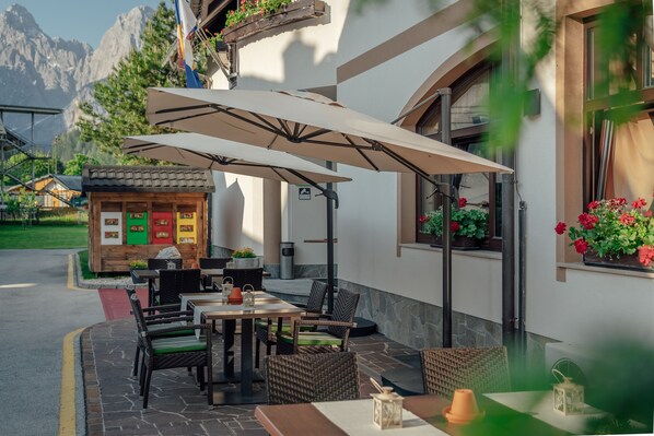 An outdoor patio with wicker furniture, a table, and a large umbrella. - Garni Hotel Miklic (Kranjska Gora)