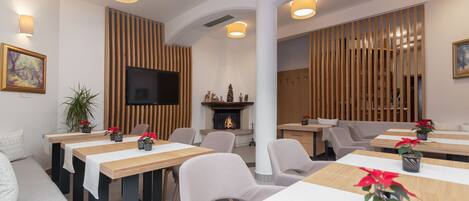 A modern dining area with wooden tables, comfortable seating, and a fireplace.