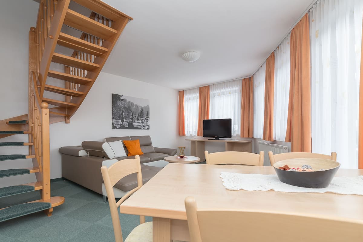 A modern living room with a wooden staircase, a sofa, a dining table, and a television.