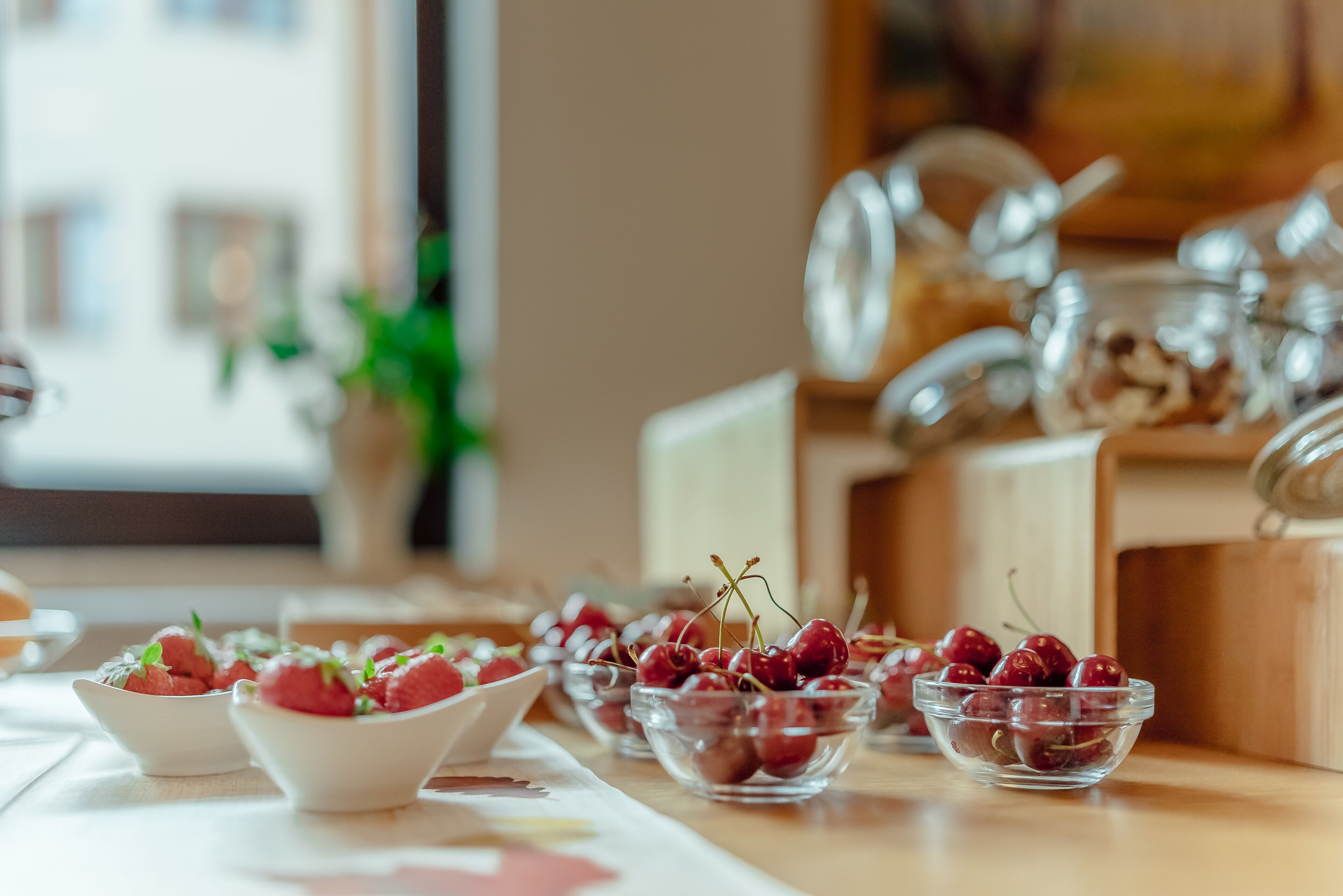 A table with multiple bowls containing cherries, a white plate, and a vase with green plants.