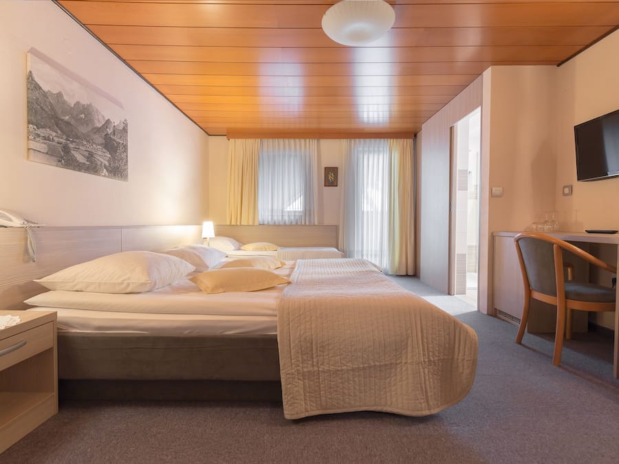 Une chambre d’hôtel avec un plafond en bois, un lit recouvert d’une courtepointe beige, un bureau avec une chaise et un téléviseur fixé au mur.
