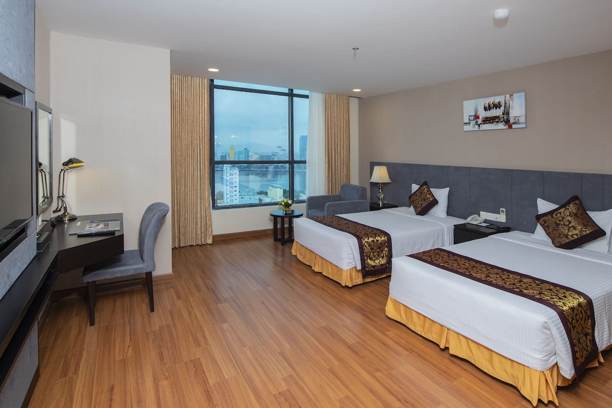A hotel room with two beds, a desk, a chair, a TV, and a large window with a city view.