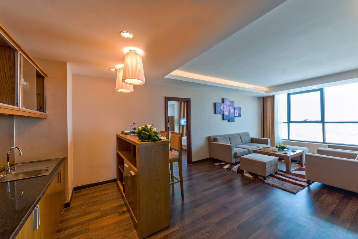 A modern living room with a sofa, coffee table, and a kitchen area with a sink and wooden cabinets.