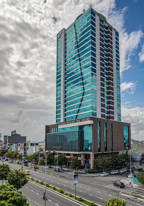 Un immeuble moderne de grande hauteur, doté d’une façade en verre, d’une entrée imposante et offrant une vue dégagée sur l’environnement urbain environnant.