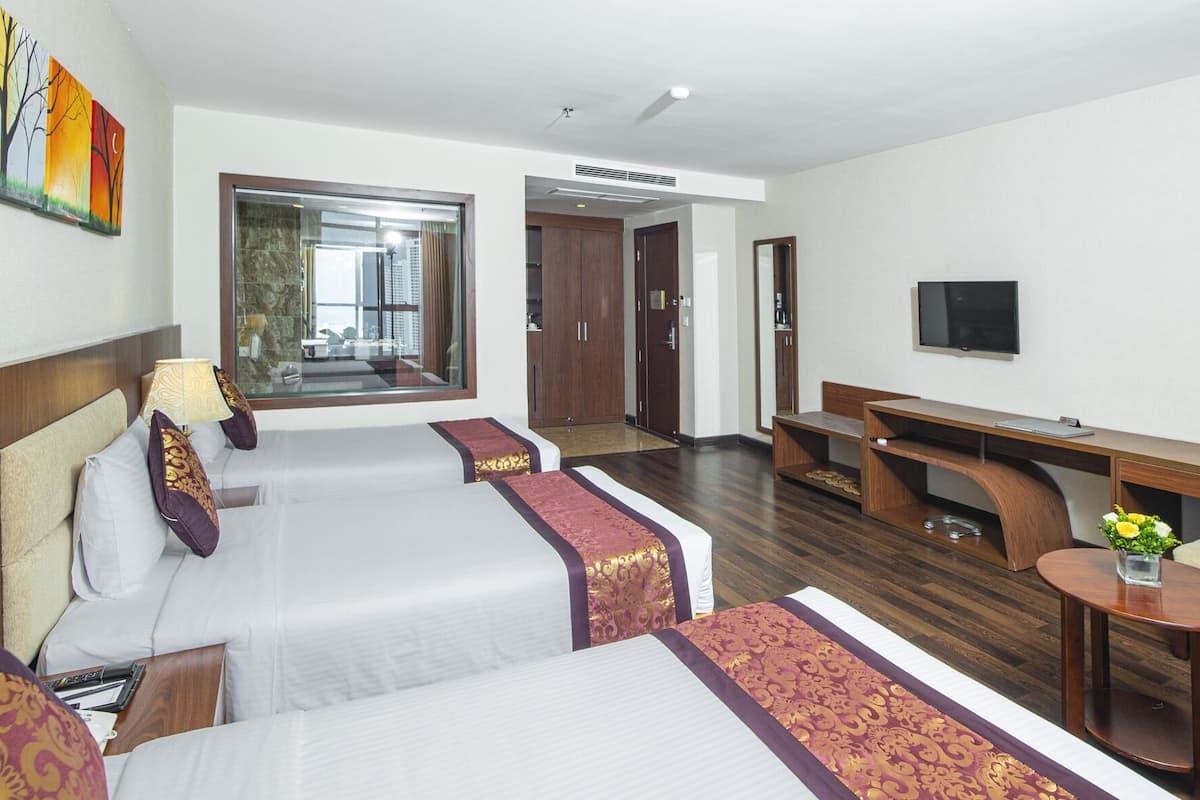 Habitación de hotel con dos camas, un escritorio, un televisor y un baño visible a través de una puerta de cristal.