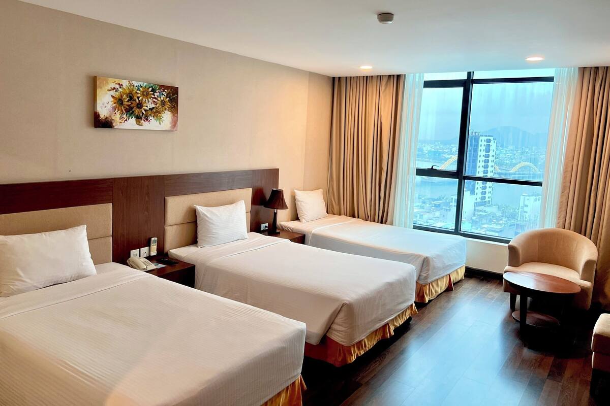 A hotel room with two beds, a desk, a chair, and a large window with a city view.