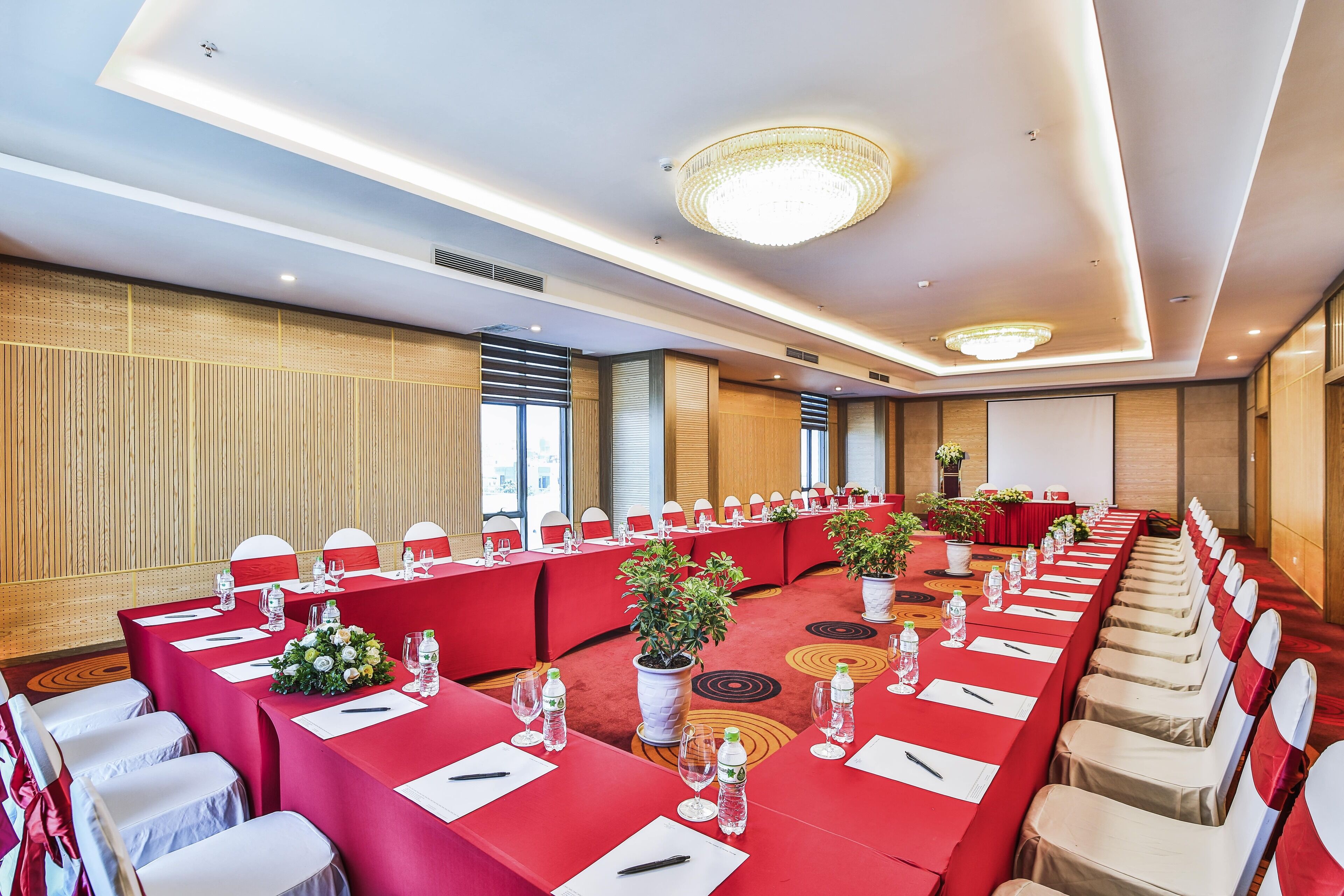 A conference room with long tables, chairs, and a large screen.